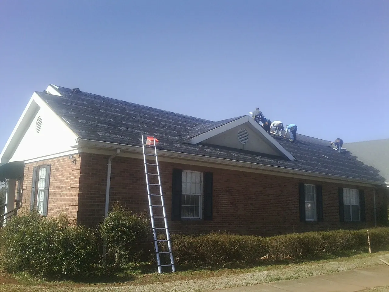 Crew tearing shingles off a brick ranch roof with a ladder set — Emergency Roof Repair work by our crew in Chaptico