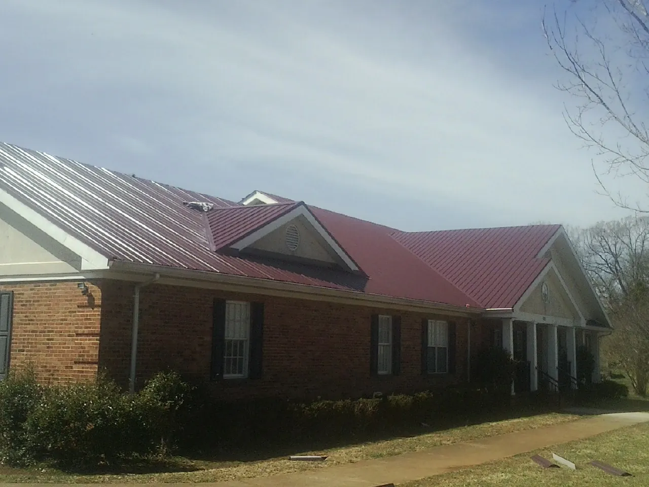 Red metal roof with gabled entries on a long brick building, from a Hail Damage Roof Repair job in Chaptico