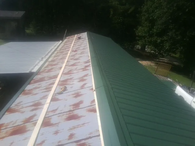 Old rusted panels beside newly installed green metal roofing — Wind Damage Roof Repair by Roofing Brothers in Chaptico