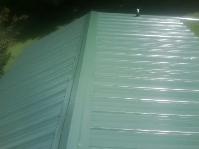 New green metal panels meeting at the ridge of a roof — Flat Roof Repair work by our crew in Chaptico
