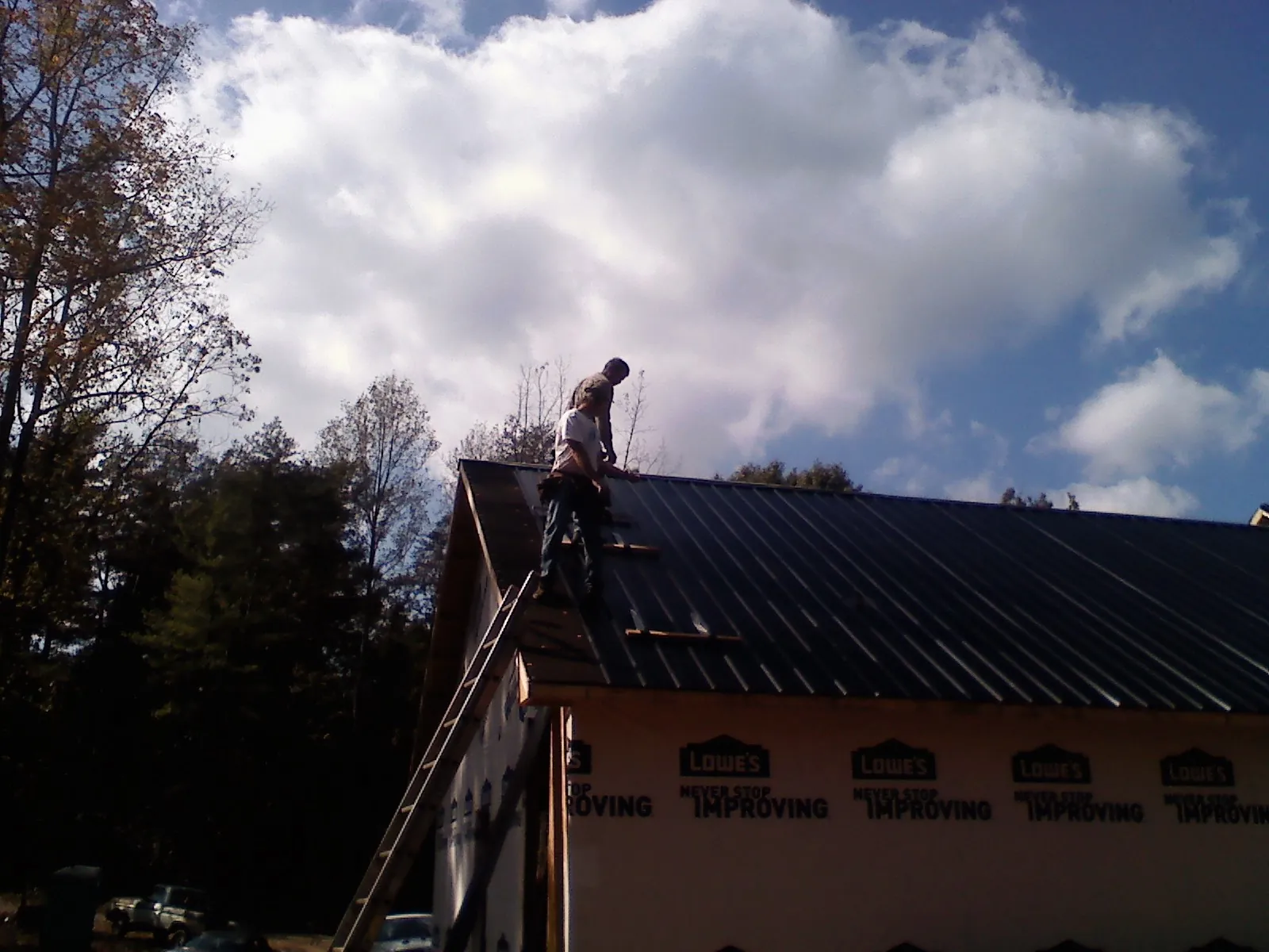 Roofer fastening dark metal panels high against a cloudy sky, from a Roof Inspection job in Chaptico